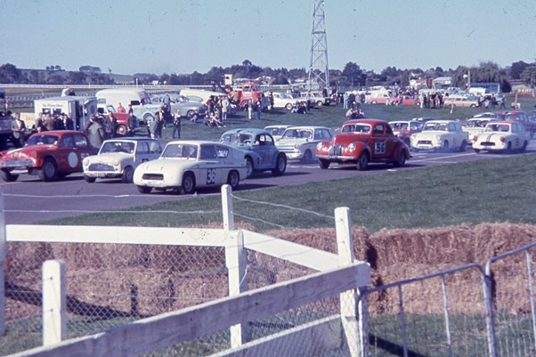Pukekohe 14 May 66 – The #52 red car on the front left is Tim Boyle in the Humber Jaguar 3.8. Frank Radisich on his #36 Lotus Anglia 1650cc is on the front right of the grid. The light blue car behind the front row is Garth Souness in his #177 Morrari 5300cc, and the red car is John Riley in the #56 Ford Corvette 4800cc – photo by Peter Levet via Milan Fistonic