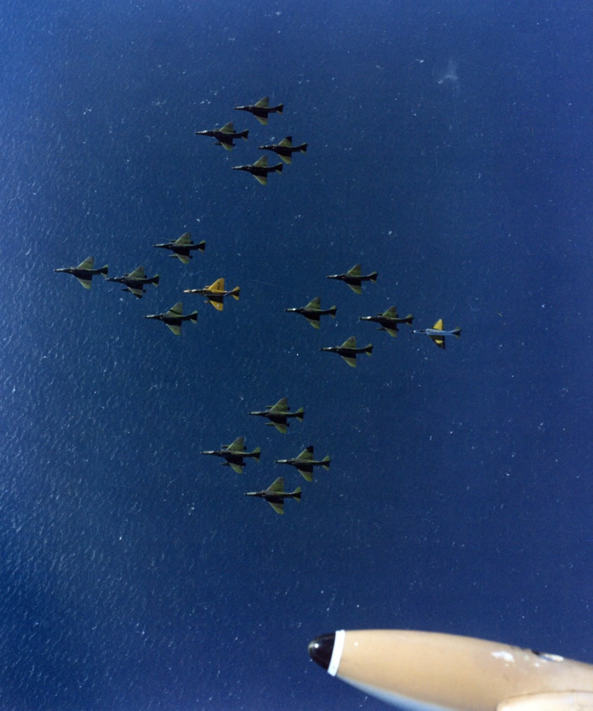 18 A4 Skyhawks in close formation. At the rear of the first flight of five Skyhawks is TA4F NZ6256 painted in a special gold colour scheme to mark the RNZAF 50th ‘Golden’ Anniversary; and the silver A4F/K NZ6215 at the rear of the formation had been stripped of paint ready for the dark green camouflage paint scheme to be applied – Photo RNZAF C252/97 8 Apr 87 taken from a 14 Squadron Strikemaster - with the fuel tip tank showing at the bottom of this photo.