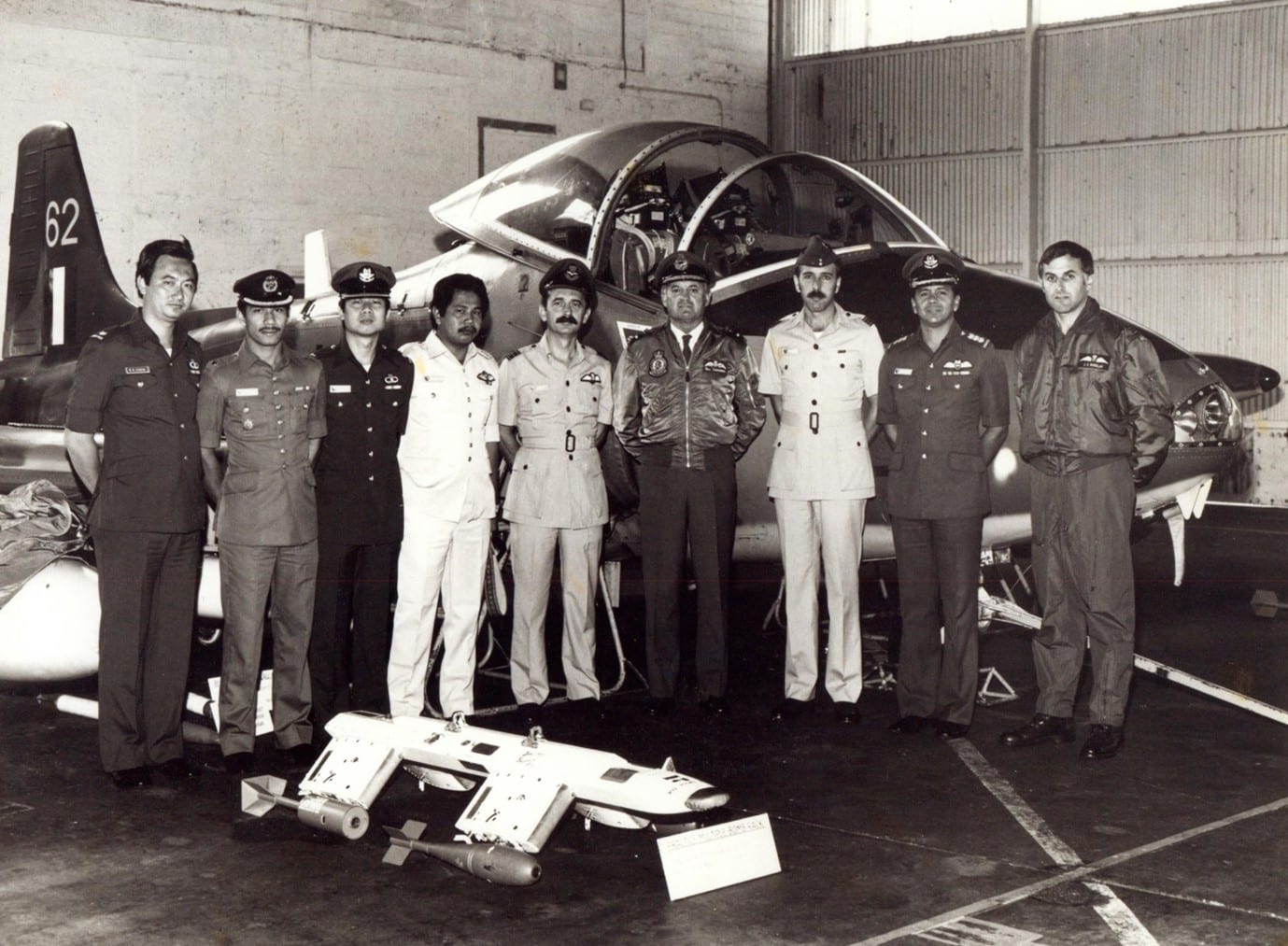 Ohakea 24 Nov 82 – Visit to 14 Sqn by AVM Symmonds RAAF, Commander IADS, and IADS staff officers. Left to R - Maj Chew RSAF, Mej Sofian Malaysian Army, Maj Mike Chuan RSAF Staff Officer (SO) Sams, Maj Bashir RMAF SO Fighters, Wg Cdr Dave Light RAF Snr Off Air Defence, AVM Symmonds RAAF, Sqn Ldr Derick Dunton RAF SO Control & Reporting, Col Tim Desouza RSAF SASO IADS, Sqn Ldr Jim Barclay CO 14 Sqn – photo RNZAF Ohakea G3308/82. In front of the visiting party is a Practice Multiple Bomb Release (PMBR) carrier that is fitted underwing to a SMR to enable the carriage of MK106 HDB and BDU33 SDB practice bombs – the two practice bombs are seen affixed to the PMBR, with the MK 106 on the rear station, and BDU33 on the front.